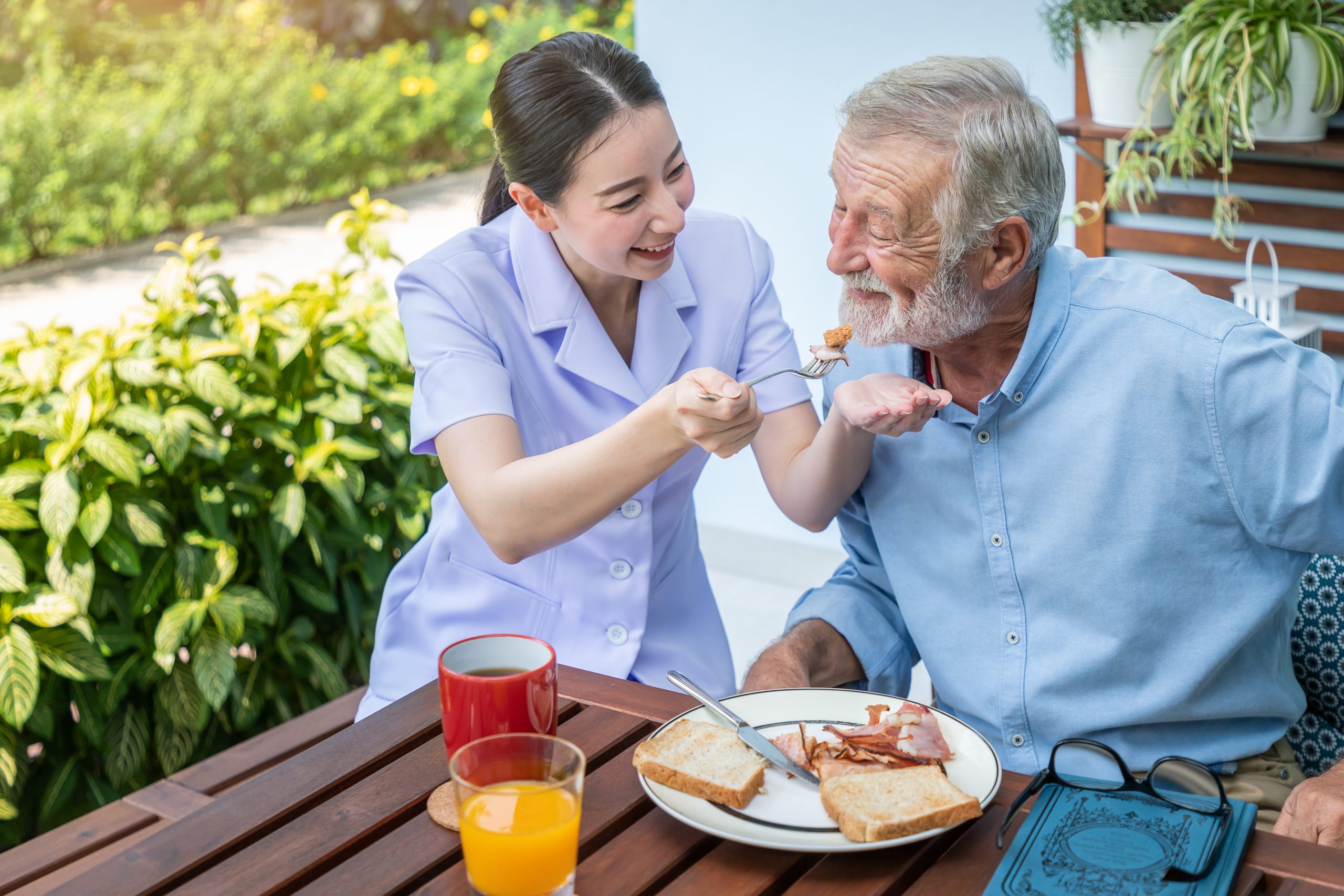 Nurse feeding elderly senior man to eat breakfast at nursing hom